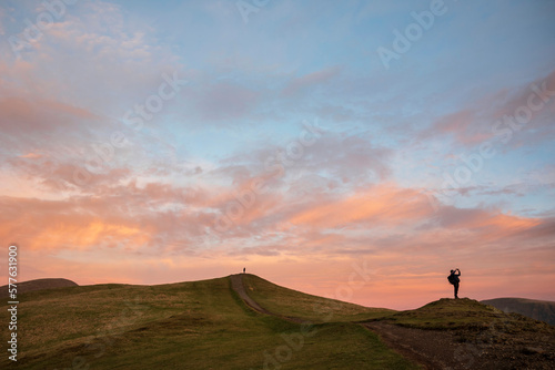 Beautiful colorful Winter sunset landscape over Latrigg Fell in Lake District with two people on hilltop admiring sunset © veneratio