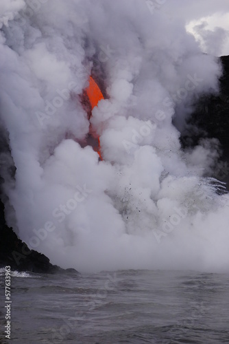 Lava flows down from high cliff into the ocean surrounded by white steam, Big Island in Hawaii