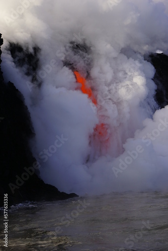 Lava flows down from high cliff into the ocean surrounded by white steam, Big Island in Hawaii
