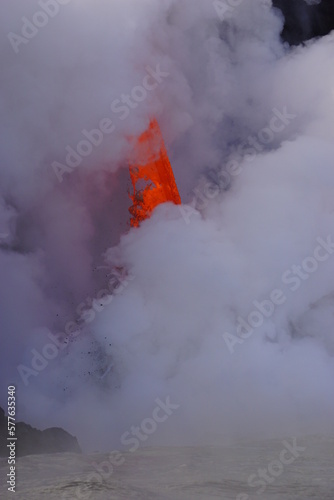 Hot lava stream flowing down from high cliff  into the ocean surrouded by white steam © Iva