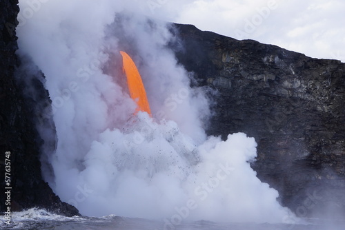 Hot lava stream flowing down from high cliff into the ocean surrouded by white steam