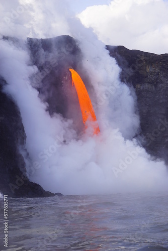 Lava flows down from high cliff into the ocean surrounded by white steam, Big Island in Hawaii