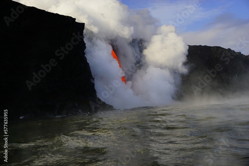 Hot lava stream flowing down from high cliff  into the ocean surrouded by white steam