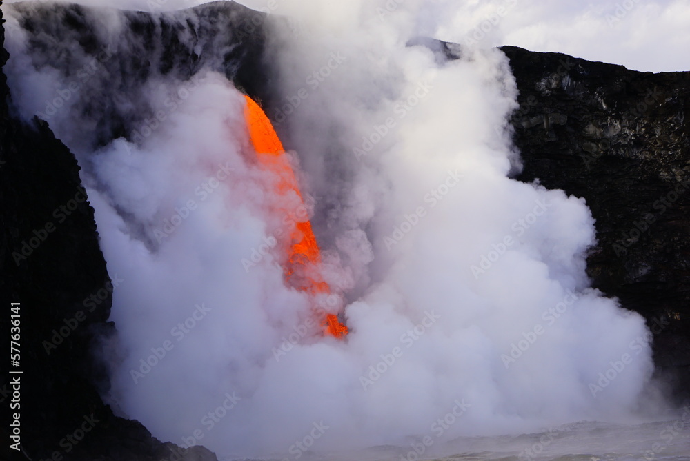 Fototapeta premium Hot lava stream flowing down from high cliff into the ocean surrouded by white steam
