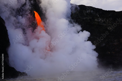 Stream of hot lava flowing down from high Cliff surrounded by white steam, Hawaii Big Island