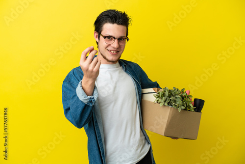 Russian Man making a move while picking up a box full of things isolated on yellow background making money gesture