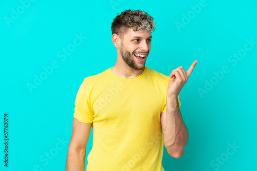 Young handsome caucasian man isolated on blue background intending to realizes the solution while lifting a finger up