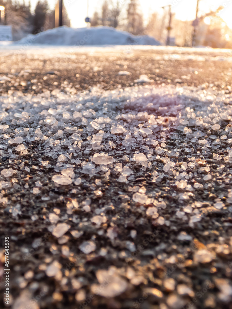 Salt grains on icy sidewalk surface in the winter. Applying salt to keep roads clear and people safe in winter weather from ice or snow. Macro view of salt grains with winter scenery in bacground Salt grains on icy sidewalk surface in the winter. Applying salt to keep roads clear and people safe in winter weather from ice or snow. Macro view of salt grains with winter scenery in bacground
