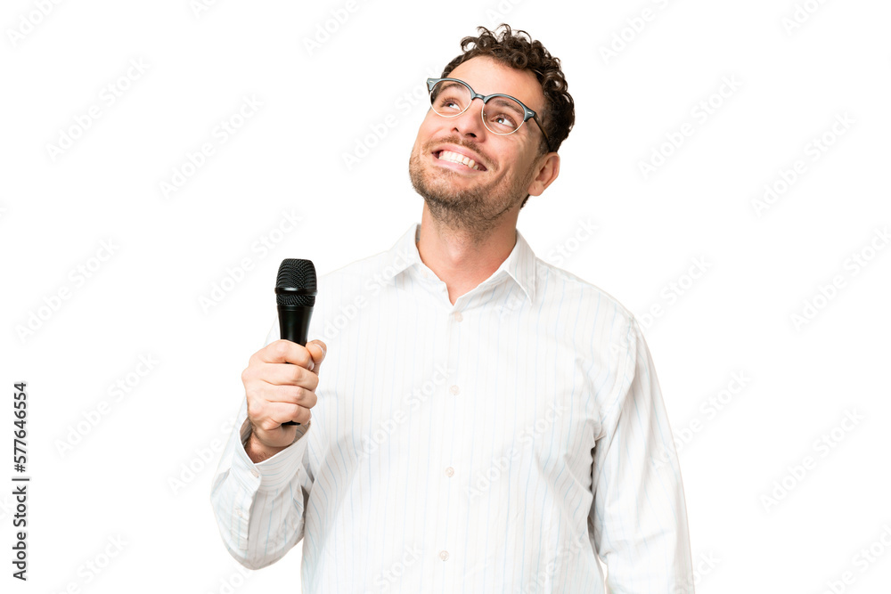 Brazilian man picking up a microphone over isolated chroma key background thinking an idea while looking up Brazilian man picking up a microphone over isolated chroma key background thinking an idea while looking up