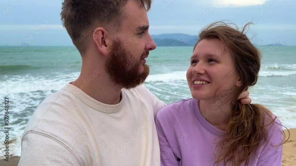 young happy couple in love on a honeymoon in bad weather, on vacation make a video selfie , sea background, the concept of a sweet relationship, kiss young happy couple in love on a honeymoon in bad weather, on vacation make a video selfie , sea background, the concept of a sweet relationship, kiss