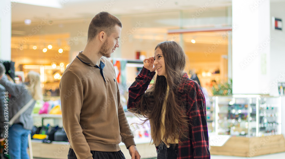 Fototapeta premium Young couple shopping in the mall. Happy couple in love at the mall. Smiling teenagers in casual clothes have fun together. They laugh, talk about buying gifts.Love, holiday sales, retail, consumerism