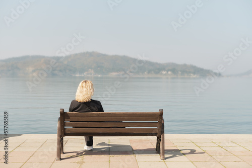 Beautiful adult woman sits after a walk on a bench and looks at the sea and blue sky, space for text idea for background © Ed