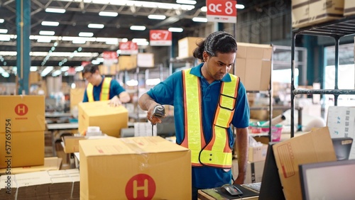 Warehouse worker using a QR code reader, scanning parcels into the system while working inside a large distribution center, worker checking goods packages and making inventory of goods