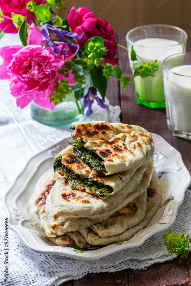 Traditional Armenian flatbread with greens zhengyalov hats, served with yogurt on the background of a bouquet.