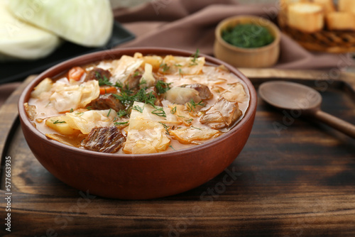 Tasty cabbage soup with meat, carrot and dill on wooden table, closeup