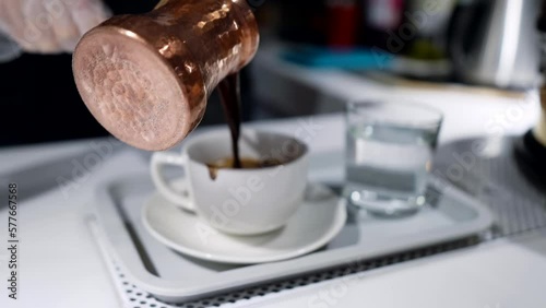 barista pouring fresh hot coffee in cup from traditional turkish copper cezve, closeup view photo