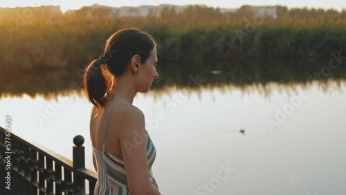 Video of young woman standing near city lake in park and enjoying sunset and beautiful weather. photo