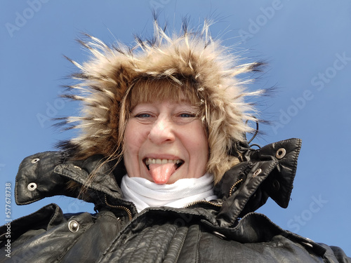 A cheerful girl or woman in a hooded jacket with fur on a sunny spring or winter day. An adult lady on a cold day © keleny