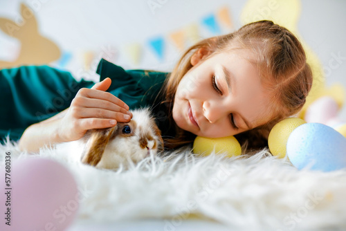 Little girl lies on the floor, strokes rabbit with her hand against the background of Easter decor photo