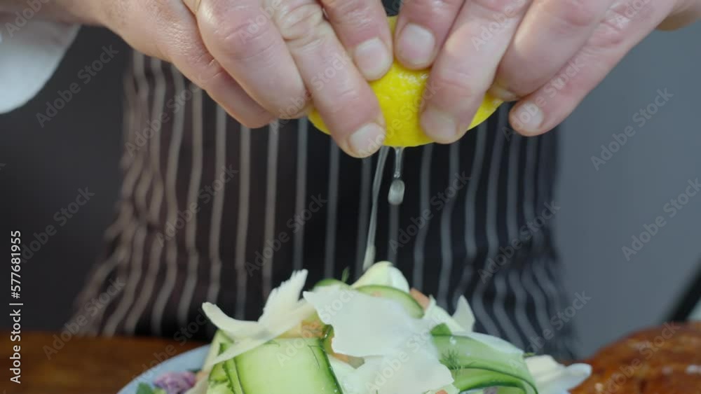 Chef squeezes a half cut lemon over a bowl of gourmet green salad. Squeezing fresh lemon. Mixed greens close up. Cooking delicious vegetarian food. Slow motion footage. Chef squeezes a half cut lemon over a bowl of gourmet green salad. Squeezing fresh lemon. Mixed greens close up. Cooking delicious vegetarian food. Slow motion footage.
