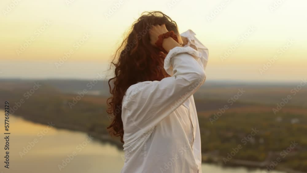 Portrait of a young pretty smiling woman standing in nature against a beautiful view at sunset in the evening, the girl straightens her curly dark hair. Portrait of a young pretty smiling woman standing in nature against a beautiful view at sunset in the evening, the girl straightens her curly dark hair.