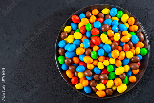 Multi-colored round candies in colored glaze in large quantities in a plate