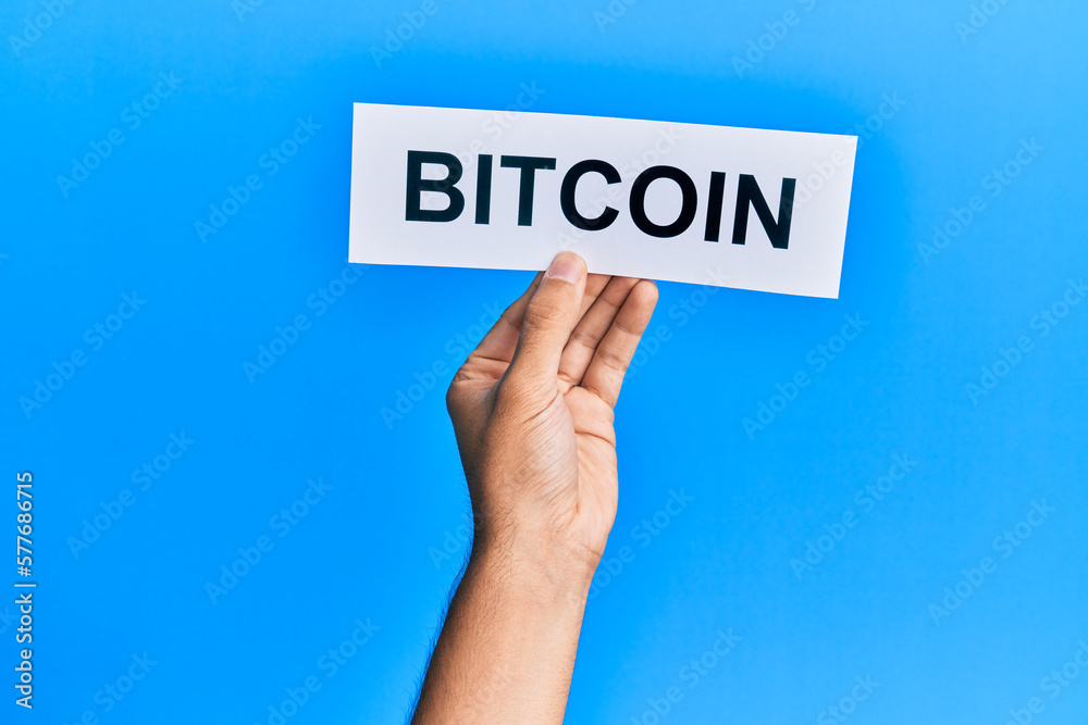 Hand of caucasian man holding paper with bitcoin word over isolated blue background