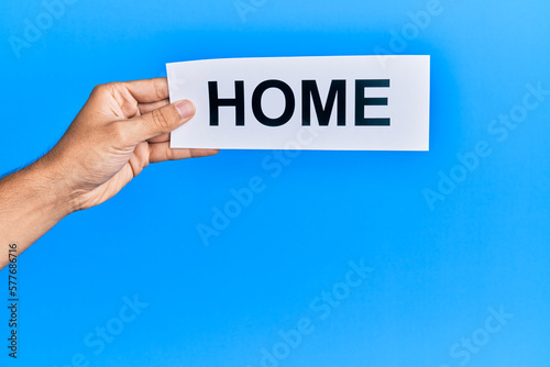 Hand of caucasian man holding paper with home word over isolated blue background