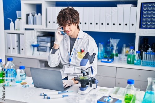 Young hispanic man scientist talking on the smartphone using laptop at laboratory