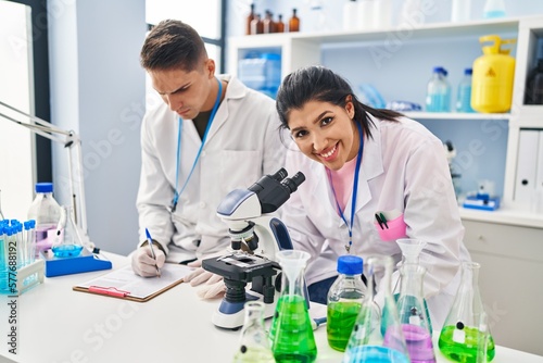 Man and woman scientists partners using microscope working at laboratory