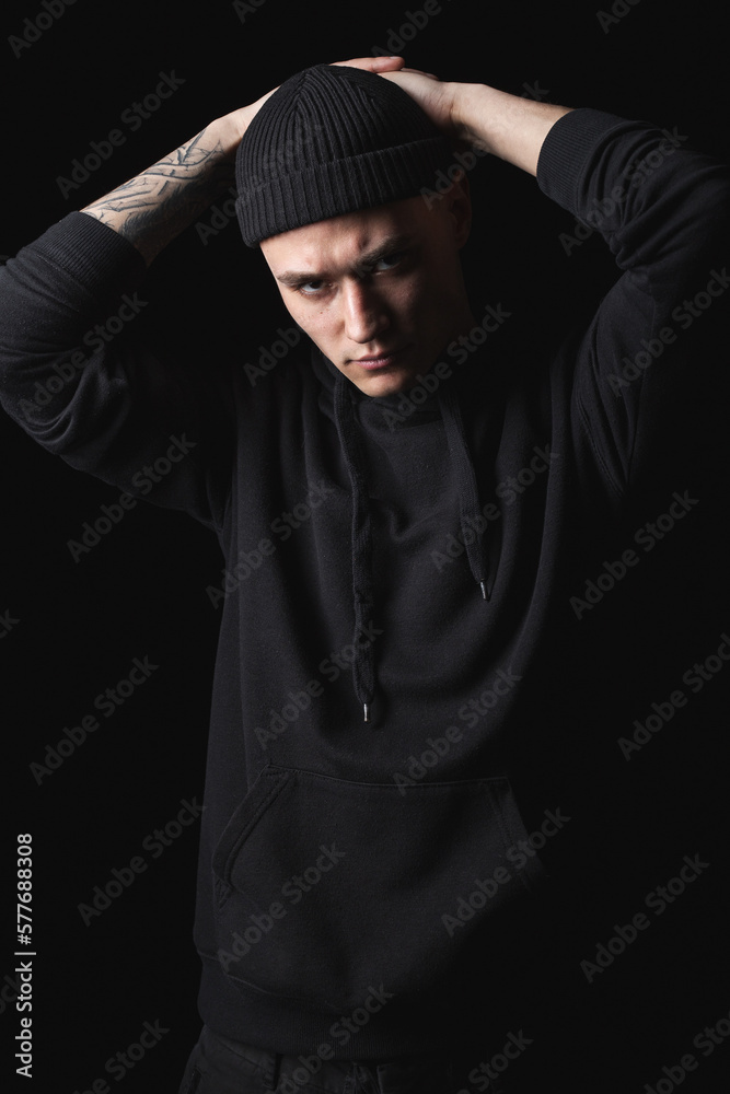 Studio portrait of handsome hipster guy wearing black blank hoodie or sweatshirt and hat. Mockup for print.