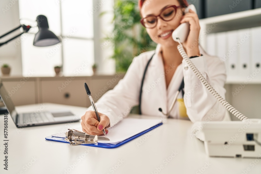Young caucasian woman doctor talking on telephone writing on document at clinic Young caucasian woman doctor talking on telephone writing on document at clinic