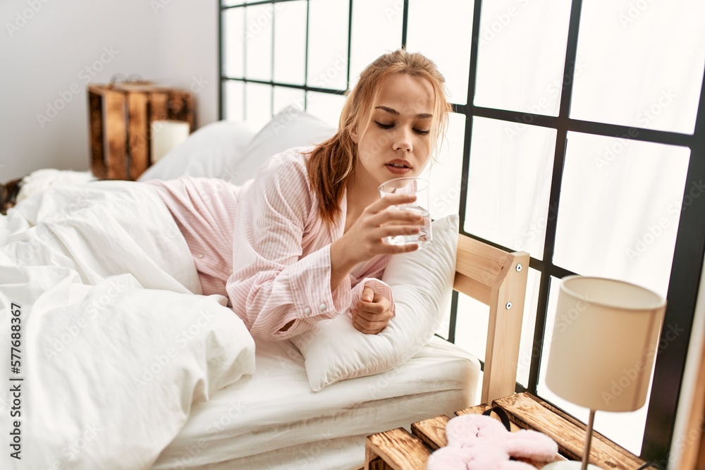 Young caucasian woman drinking glass of water lying on bed at bedroom Young caucasian woman drinking glass of water lying on bed at bedroom