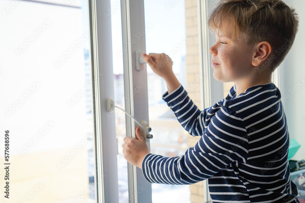 safety at home for small children. a lock on the window protects children from opening the window. The boy tries to open the window standing on the windowsill on a high floor. safety at home for small children. a lock on the window protects children from opening the window. The boy tries to open the window standing on the windowsill on a high floor.