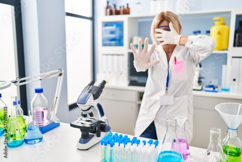 Middle age blonde woman working at scientist laboratory covering eyes with hands and doing stop gesture with sad and fear expression. embarrassed and negative concept.