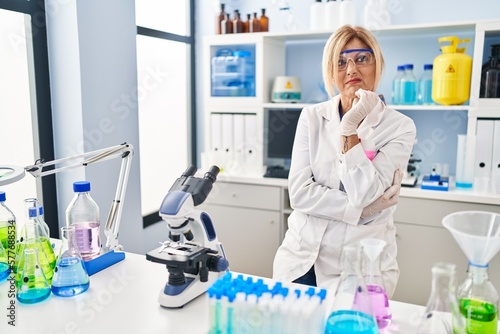 Middle age blonde woman working at scientist laboratory thinking looking tired and bored with depression problems with crossed arms.
