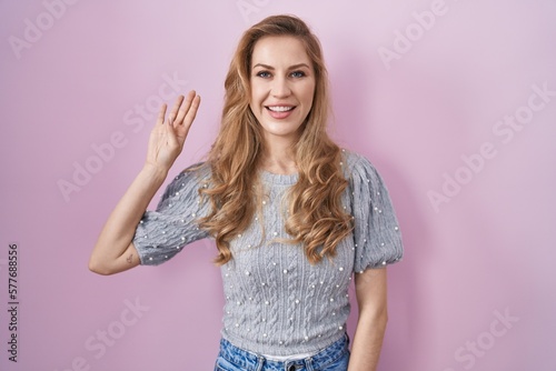 Beautiful blonde woman standing over pink background showing and pointing up with fingers number four while smiling confident and happy.