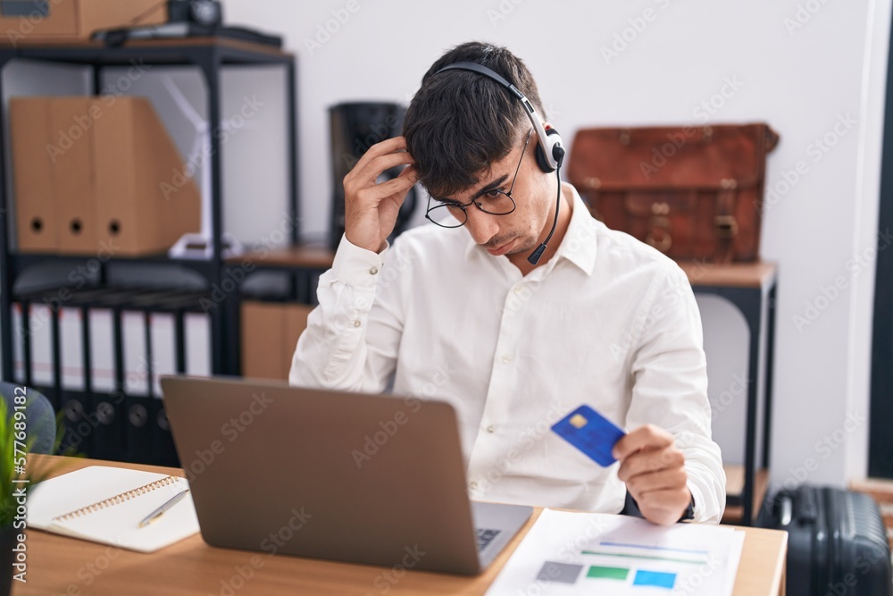 Young hispanic man working using computer laptop holding credit card worried and stressed about a problem with hand on forehead, nervous and anxious for crisis Young hispanic man working using computer laptop holding credit card worried and stressed about a problem with hand on forehead, nervous and anxious for crisis