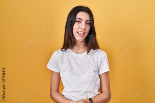 Young beautiful woman standing over yellow background with hands together and crossed fingers smiling relaxed and cheerful. success and optimistic
