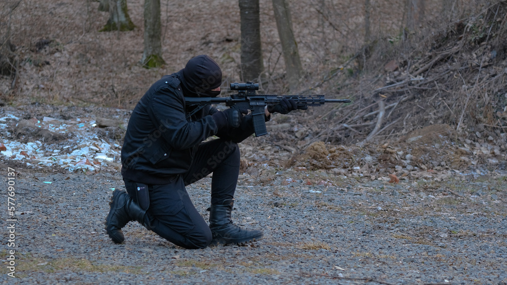Fototapeta premium A soldier of a special unit in a black uniform shoots an assault rifle at a training ground