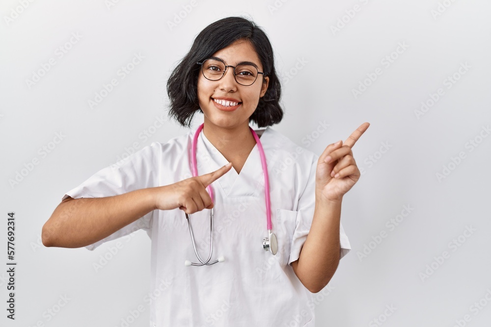 Young hispanic doctor woman wearing stethoscope over isolated background smiling and looking at the camera pointing with two hands and fingers to the side. Young hispanic doctor woman wearing stethoscope over isolated background smiling and looking at the camera pointing with two hands and fingers to the side.
