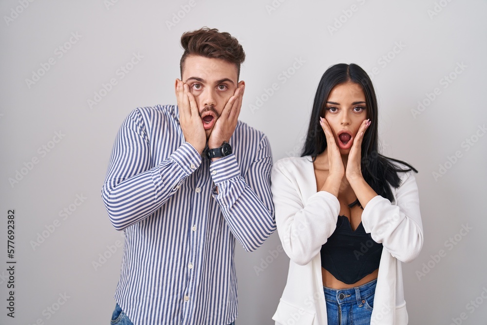 Young hispanic couple standing over white background afraid and shocked, surprise and amazed expression with hands on face Young hispanic couple standing over white background afraid and shocked, surprise and amazed expression with hands on face