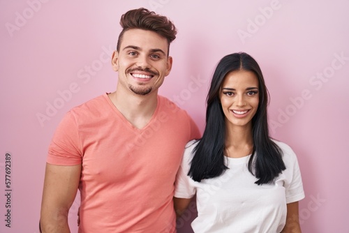 Young hispanic couple standing over pink background with a happy and cool smile on face. lucky person.