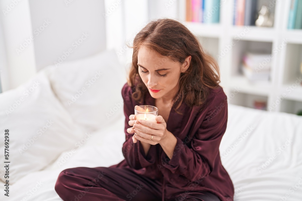 Young beautiful hispanic woman sitting on bed smelling aromatic candle at bedroom Young beautiful hispanic woman sitting on bed smelling aromatic candle at bedroom
