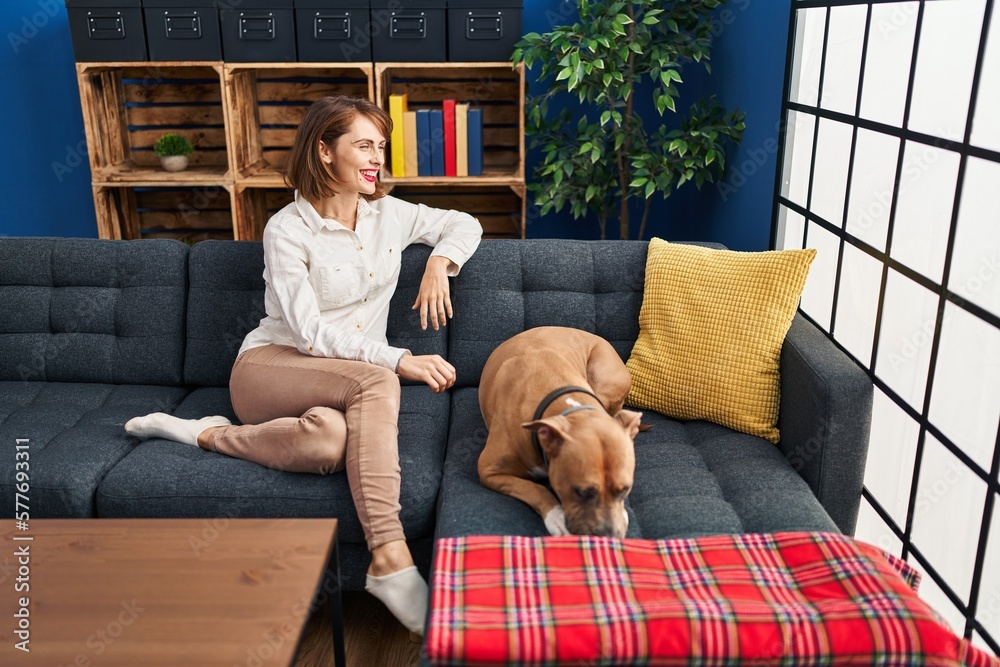 Obraz premium Young caucasian woman smiling confident sitting on sofa with dog at home