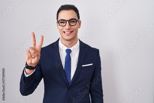 Young hispanic man wearing suit and tie showing and pointing up with fingers number two while smiling confident and happy.