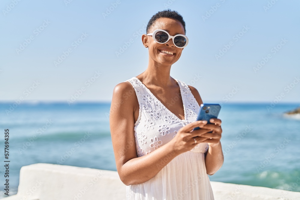 African american woman smiling confident using smartphone at seaside