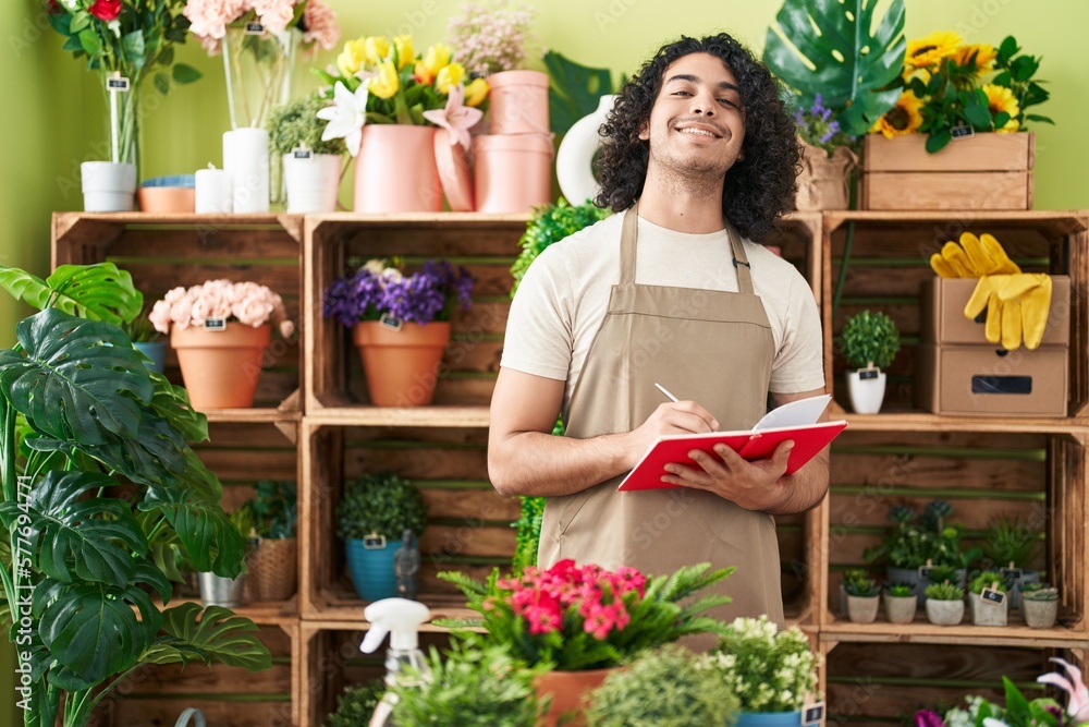 Young latin man florist smiling confident writing on notebook at flower shop