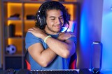 Hispanic man with curly hair playing video games hugging oneself happy and positive, smiling confident. self love and self care