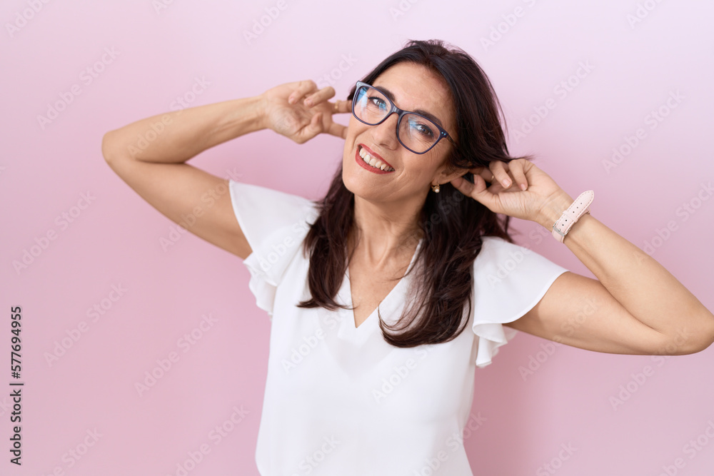 Middle age hispanic woman wearing casual white t shirt and glasses smiling pulling ears with fingers, funny gesture. audition problem Middle age hispanic woman wearing casual white t shirt and glasses smiling pulling ears with fingers, funny gesture. audition problem